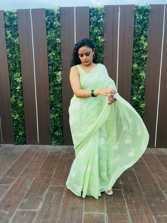 Woman in a Pista green saree standing outdoors with a wooden fence and greenery in the background
